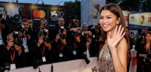 a celebrity is waving her hand on the red carpet while smiling and photographers are taking photos of her.