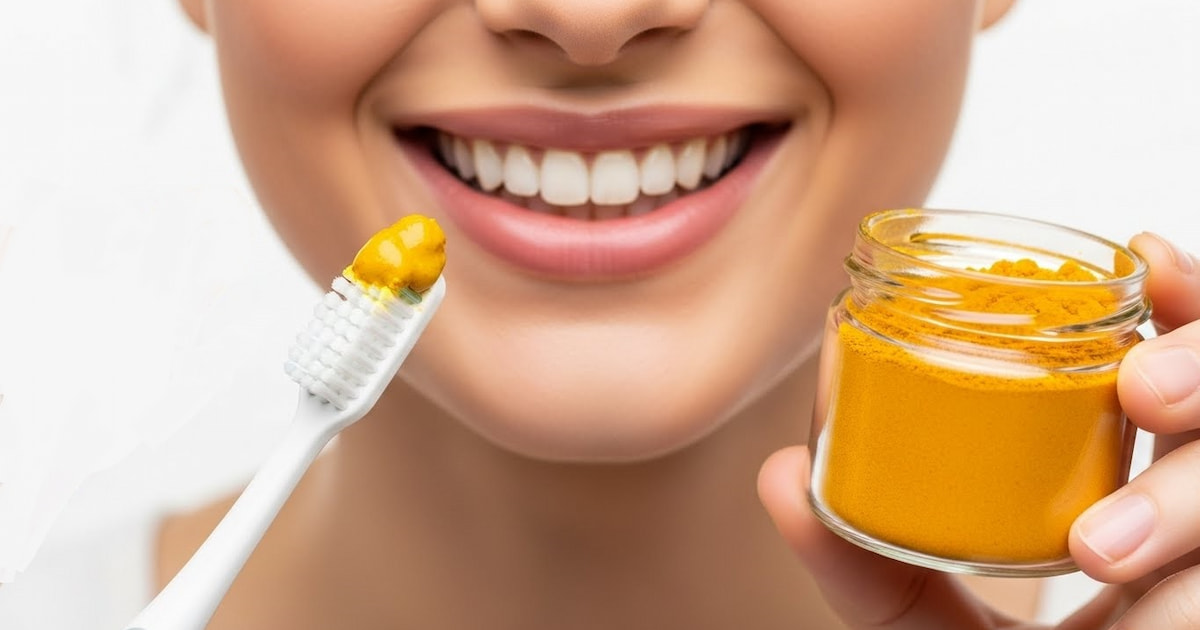 a close-up of a bright smile holding turmeric paste on a brush and turmeric powder, representing the benefit of turmeric for teeth.
