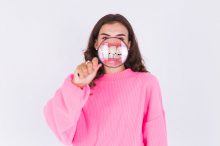a girl holding a magnifying glass in front of her mouth, revealing her red and swollen gums through the lens.