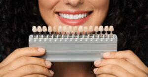 a woman is smiling and holding a set of different types of veneers in front of her teeth.
